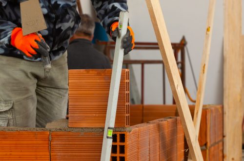 Bricklayer industrial worker installing brick masonry on interior wall with trowel putty knife